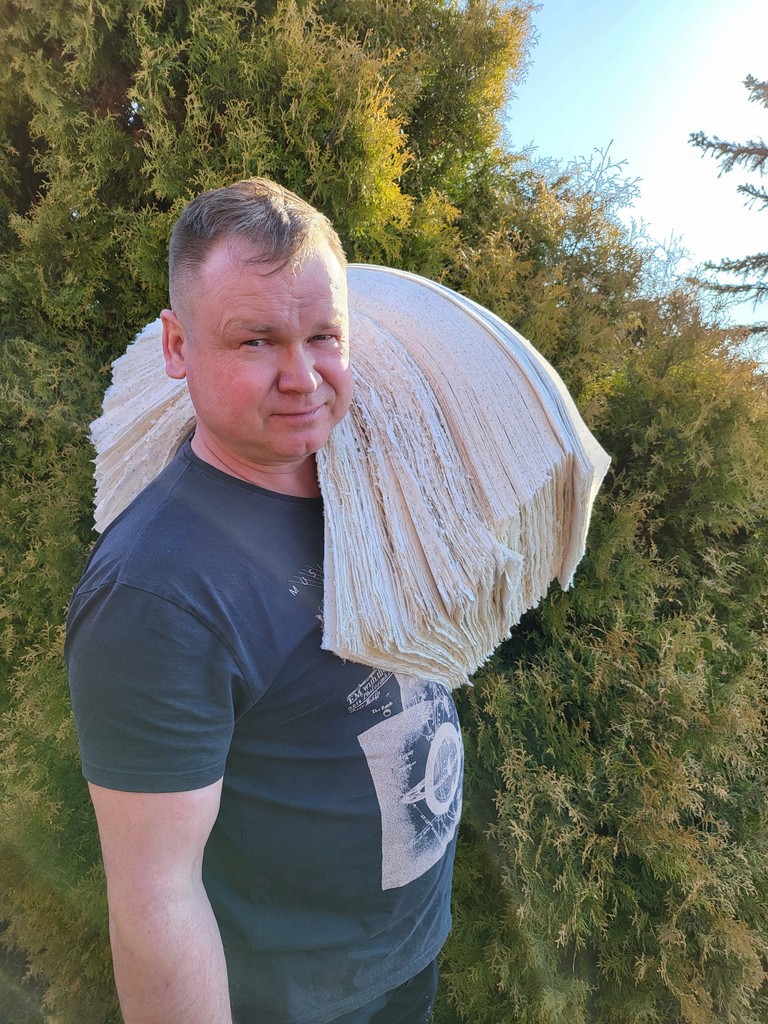 Flawiusz Pietrzyk niosący na ramieniu stos arkuszy papieru czerpanego