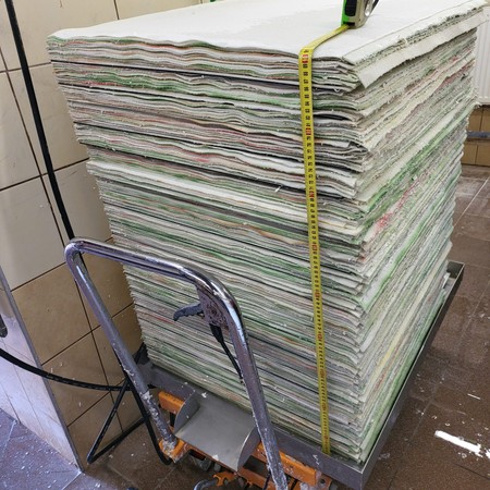 A tall stack of pressed handmade paper sheets on a trolley at the ART-PAPIER mill